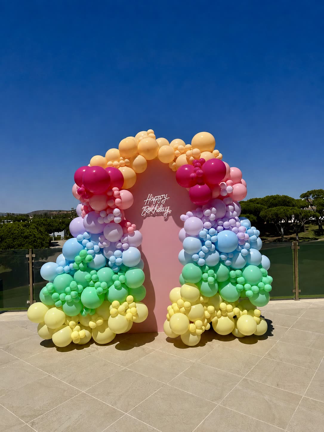 Arco de balões em tons pastel arco-íris com painel rosa de aniversário