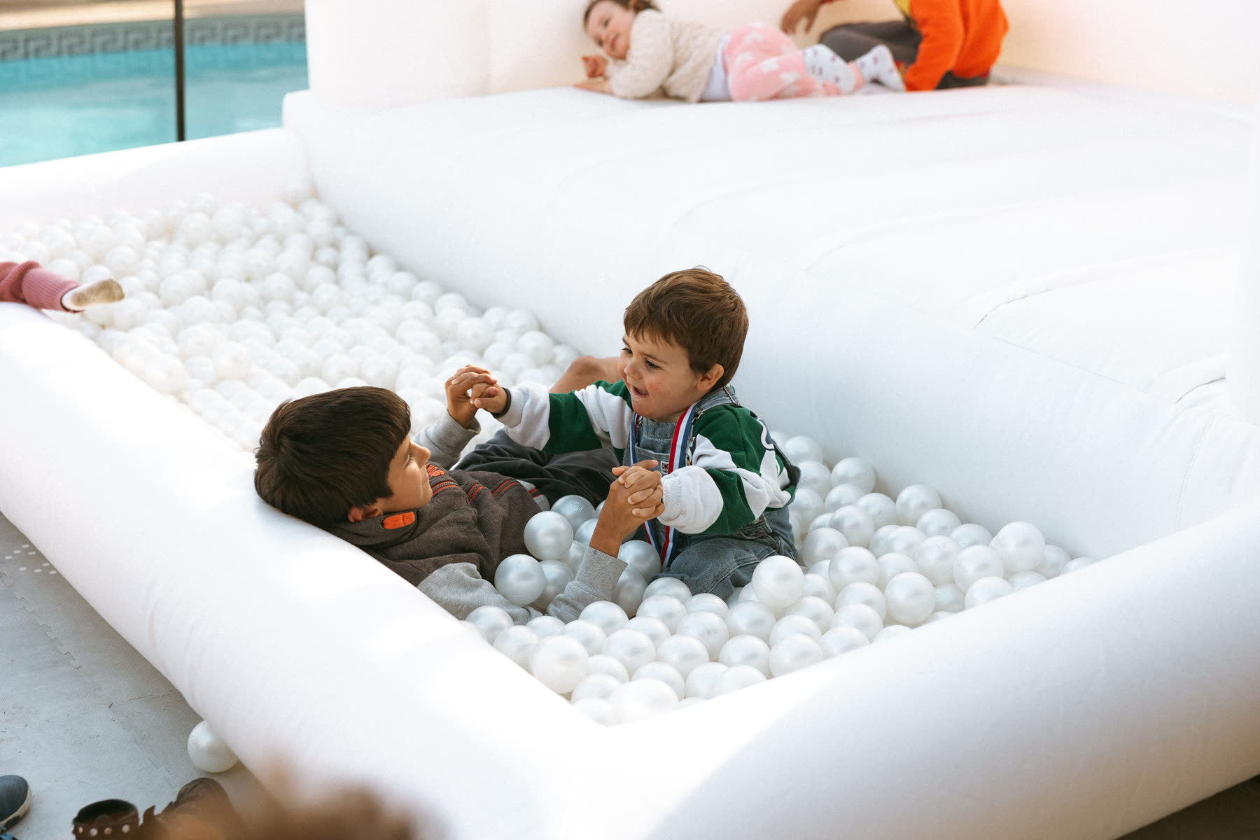 Crianças a brincar numa piscina de bolas brancas de soft play junto à piscina