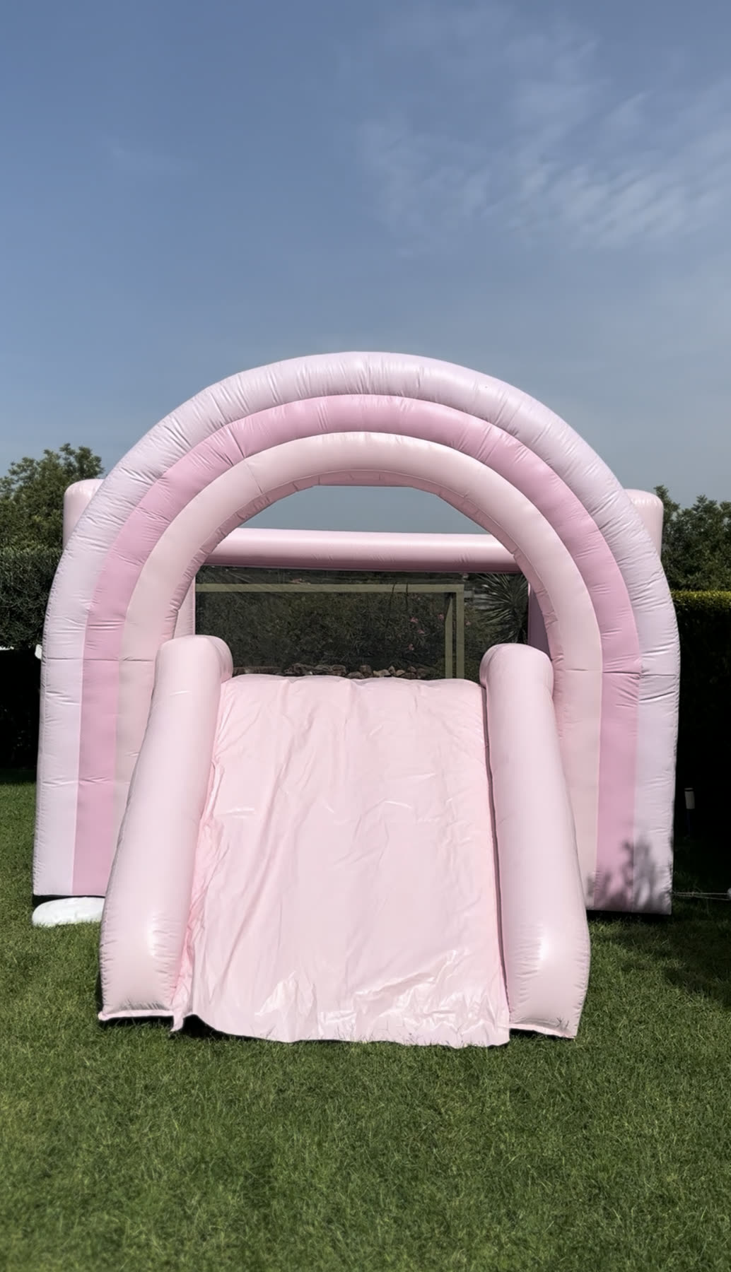 Insuflável rosa pastel com escorrega montado na relva de um jardim